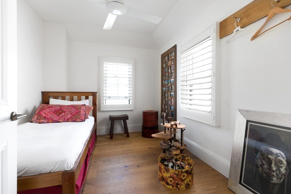 Un dormitorio con una cama, cabecera de madera, un taburete pequeño, un armario de madera y una obra de arte enmarcada en la pared.