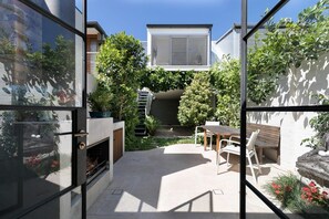 A modern outdoor patio with a dining area, a fire pit, and a view of a neighboring building.