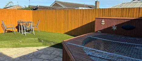 A backyard with a wooden fence, a small patio with stone tiles, and a hot tub.