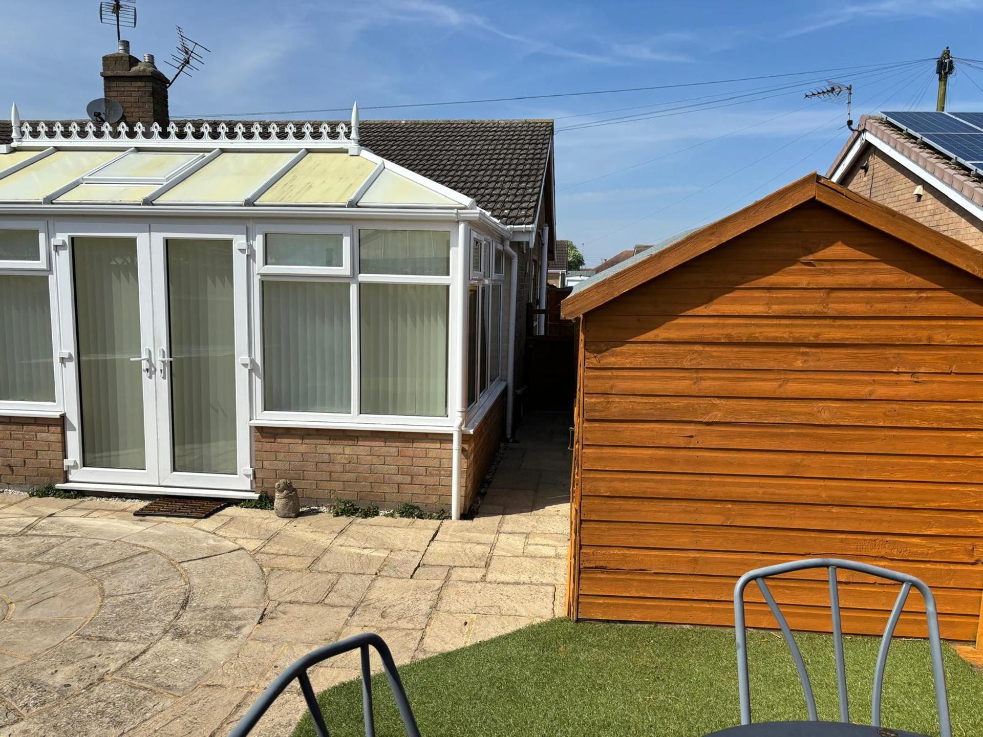 Une maison avec une véranda, un abri de jardin en bois et une terrasse dallée.