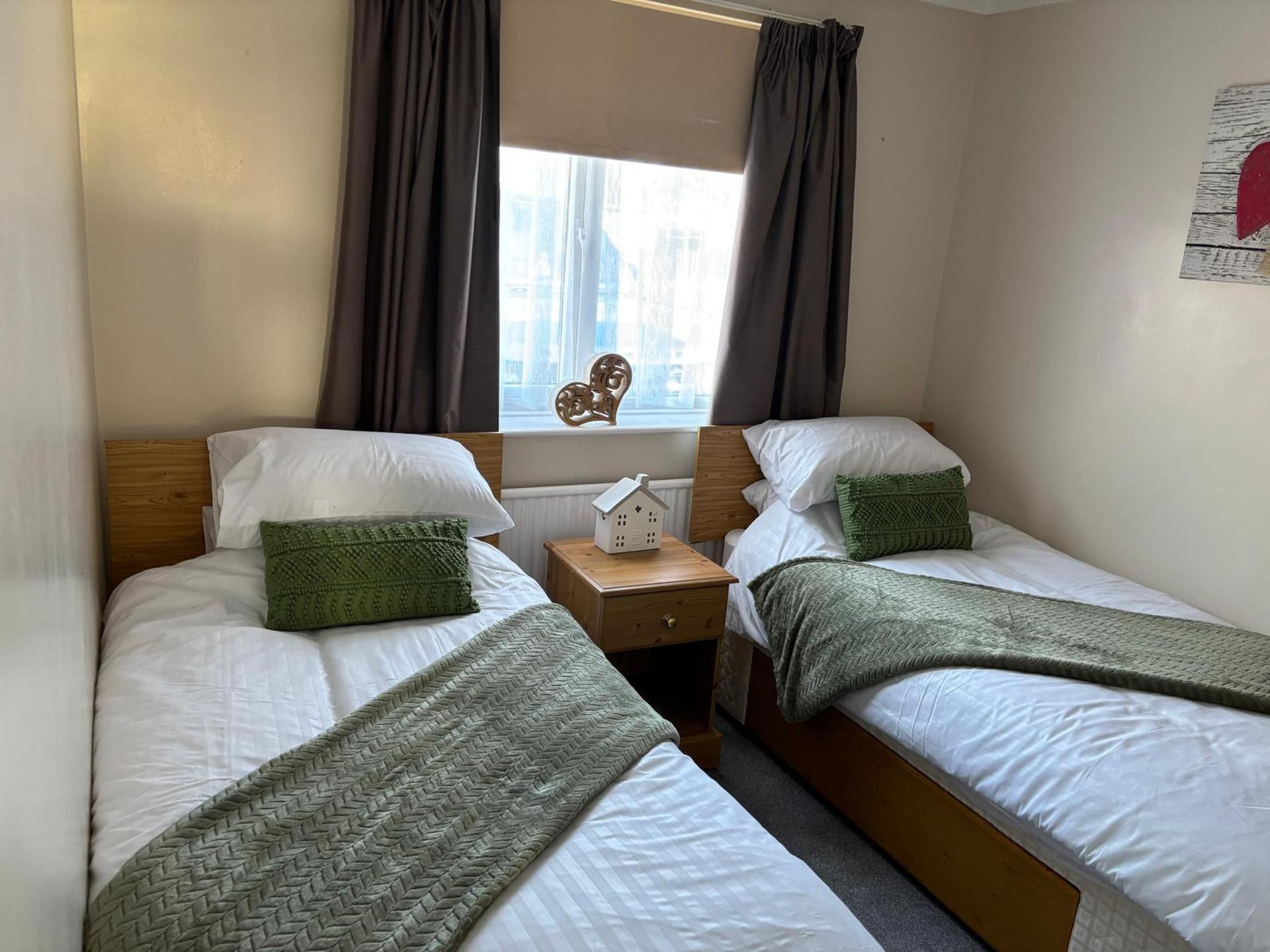 A twin room with two beds, a nightstand, a window with curtains, and a wall-mounted decoration.
