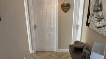 Un pasillo con una puerta blanca, suelo de madera, un cartel en la pared y una escultura.