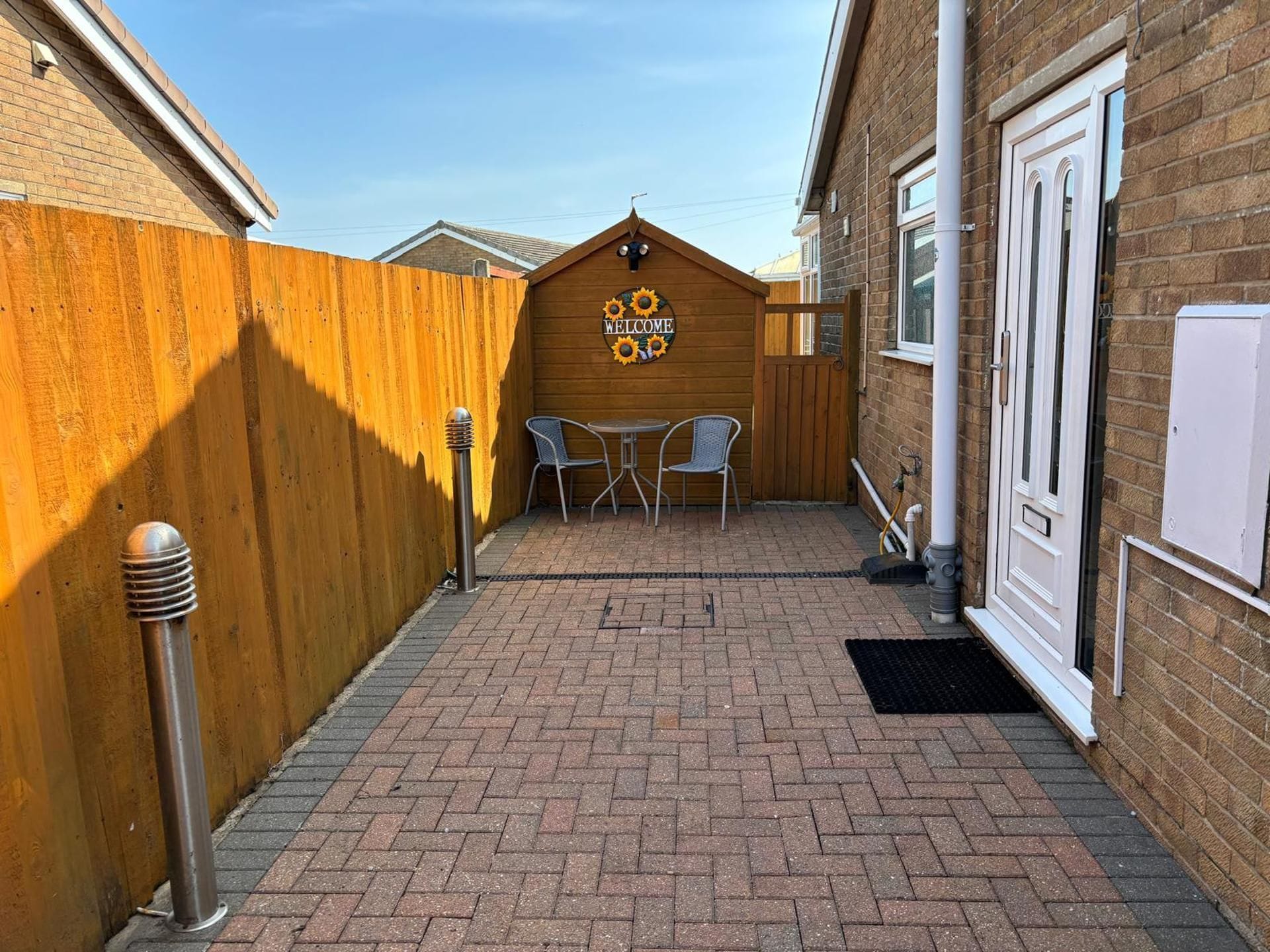 A patio area with a wooden fence, a welcome sign, two metal chairs, and a table.