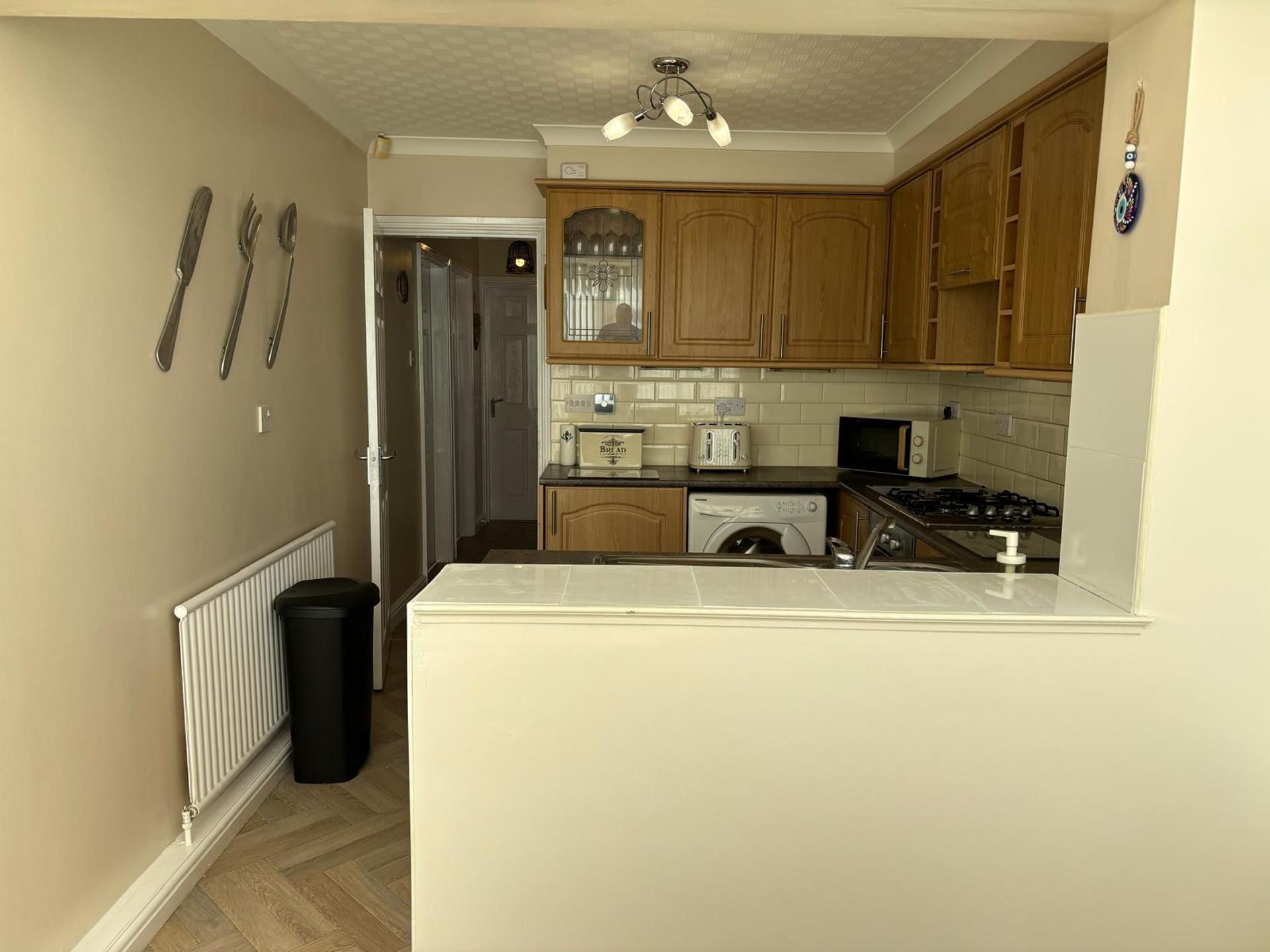 A kitchen with wooden cabinets, a built-in oven, a microwave, a toaster, and a trash bin.