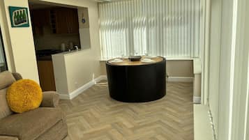 Una sala de estar moderna con piso de espiga, una mesa de centro negra redonda y una zona de comedor con mesa y sillas blancas.
