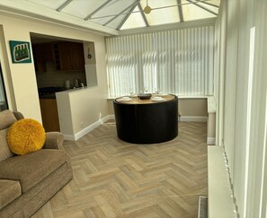 A modern living room with a herringbone floor, a round black coffee table, and a dining area with a white table and chairs. - 2-bed Bungalow, Sleeps 6, Parking & Pet Friendly (Skegness)