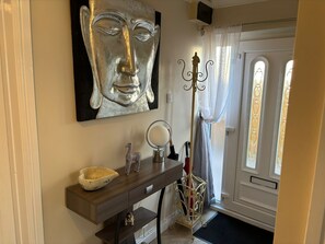 Un couloir orné d’un grand tableau abstrait, d’une console en bois sur laquelle repose un bol, d’un miroir et d’un porte-parapluie décoratif.