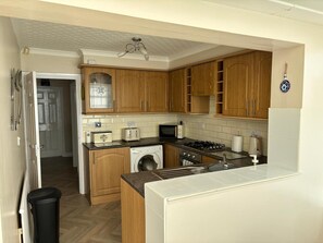 A compact kitchen with wooden cabinets, a washing machine, a microwave, and a gas stove. - 2-bed Bungalow, Sleeps 6, Parking & Pet Friendly (Skegness)