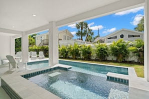 Une piscine avec un jacuzzi, entourée de colonnes blanches et offrant une vue sur les maisons voisines et les palmiers.