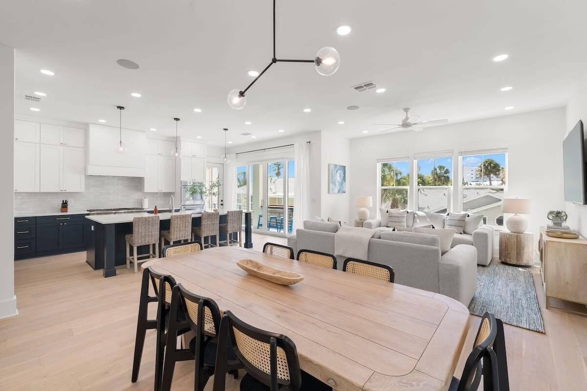 A modern kitchen with a dining area, large windows, and a view of the outdoors.