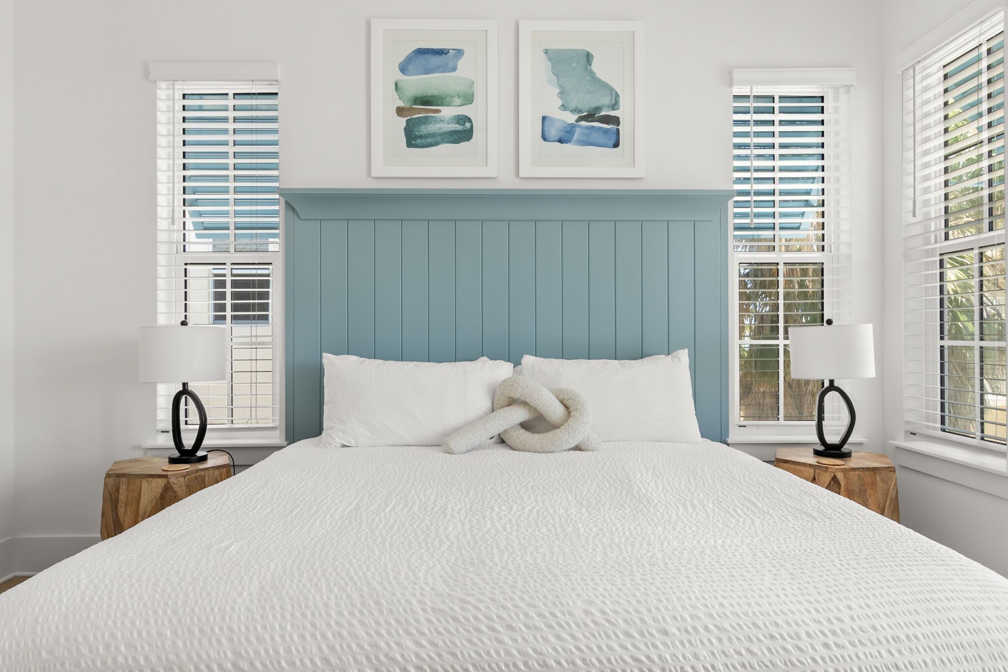 A neatly made bed with white linens, a blue headboard, and two bedside tables with lamps.
