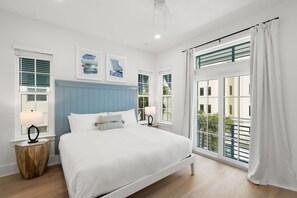 A bedroom with a bed, two bedside tables, a window with curtains, and a view of the outside.