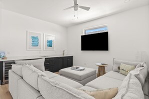 A modern living room with a grey sofa, a small ottoman, and a flat-screen TV mounted on the wall.