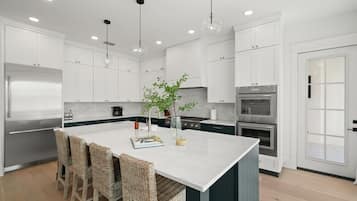 A modern kitchen with white cabinetry, a central island with bar stools, stainless steel appliances, and pendant lighting.