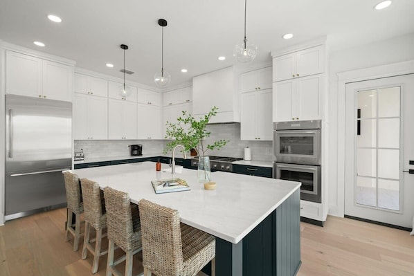 A modern kitchen with white cabinetry, a central island with bar stools, stainless steel appliances, and pendant lighting.
