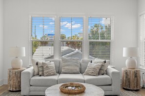 Ein Wohnzimmer mit grauem Sofa, zwei Beistelltischen mit Lampen und Blick durch große Fenster.