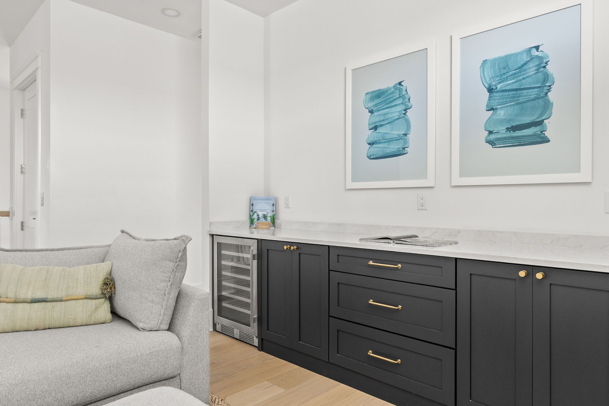 A modern kitchen with dark cabinets, a white countertop, and two framed artworks on the wall.