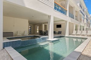 A swimming pool with a tiled deck, lounge chairs, and a covered seating area with tables.