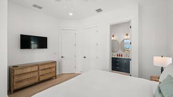 A bedroom with a bed, a television, a dresser, a vanity with a mirror, and a ceiling fan.