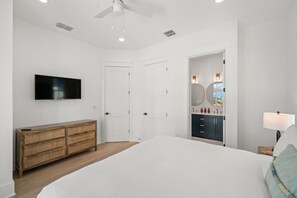 A bedroom with a bed, a television, a dresser, a vanity with a mirror, and a ceiling fan.