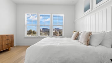 A bedroom with a large bed, a wooden dresser, and a window with a city view.