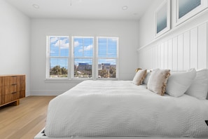 Ein Schlafzimmer mit einem großen Bett, einer hölzernen Kommode und einem Fenster mit Blick auf die Stadt.