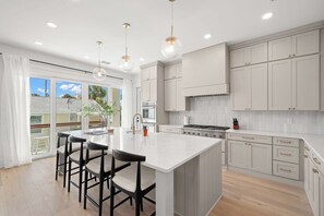 A modern kitchen with a central island, bar stools, and pendant lighting. - Pearl House at The Gemma (Clearwater)