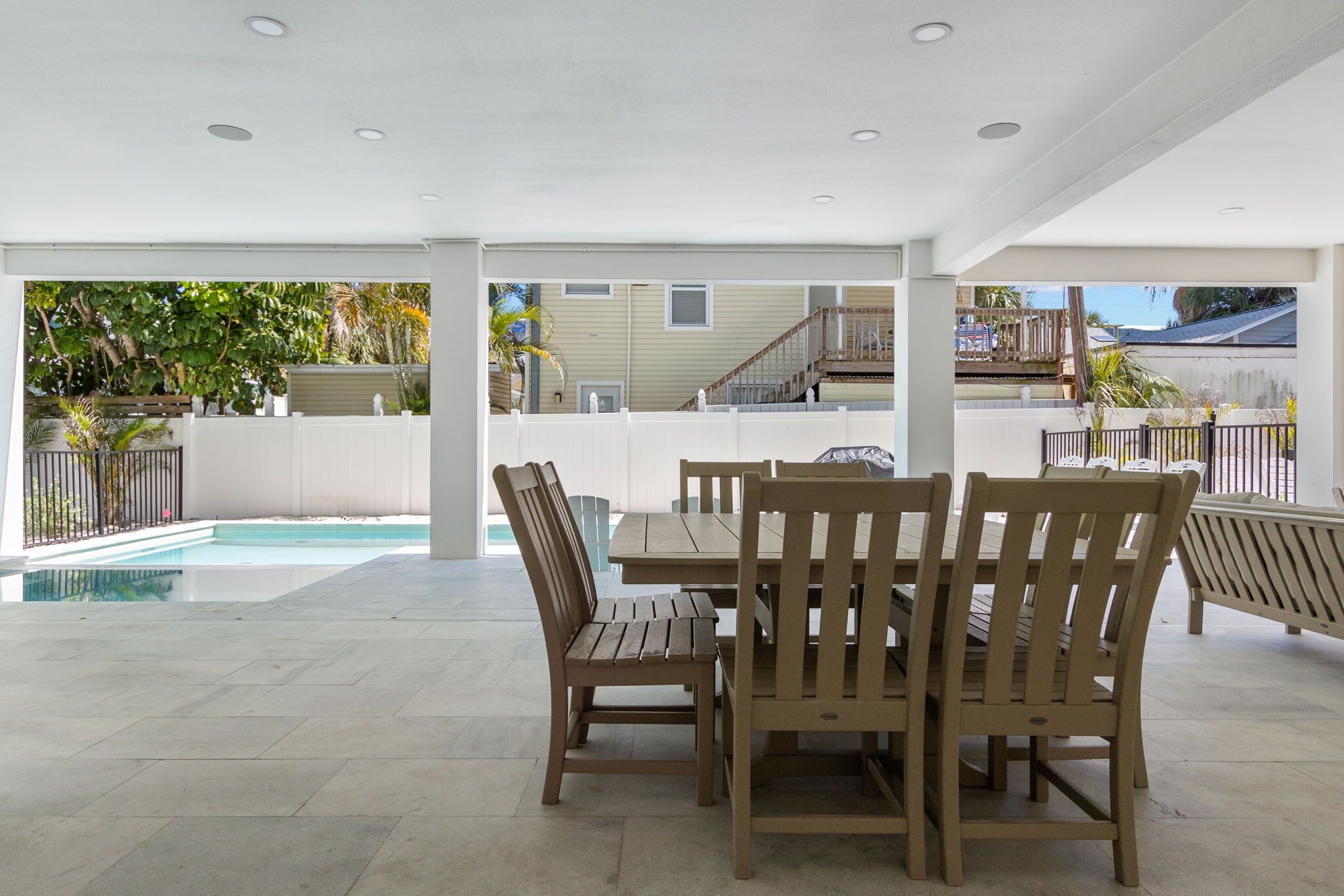 Un patio couvert avec une piscine, des meubles en bois et une vue sur un immeuble d’habitation.