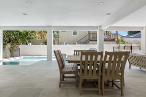 Ein überdachter Patio-Bereich mit Pool, Holzmöbeln und Blick auf ein Wohngebäude.