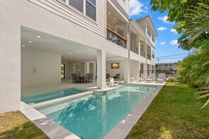 A modern two-story house with a swimming pool, outdoor seating, and a balcony.