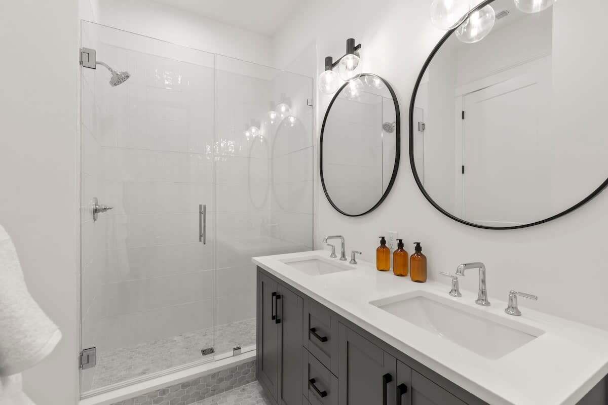 Une salle de bain moderne avec une douche à parois de verre, deux lavabos et deux grands miroirs.