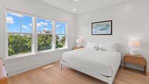 A bedroom with a large bed, two bedside tables, a ceiling fan, and a window with a view of greenery.
