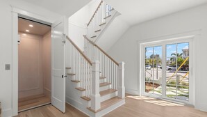 Ein modernes Interieur mit einer Holztreppe, einer Schiebeglastür zum Balkon und einer deckenebnen Leuchte.