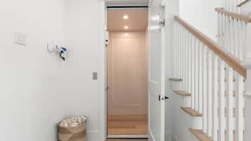 A hallway with a wooden floor, a white wall, a white door, and a white staircase with wooden steps.