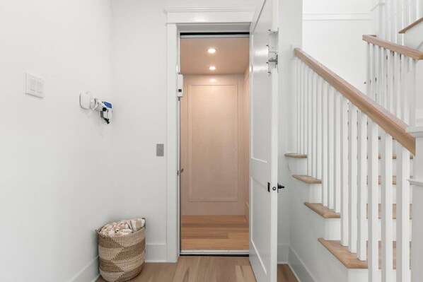 Un pasillo con piso de madera, pared blanca, puerta blanca y escalera de madera con peldaños.