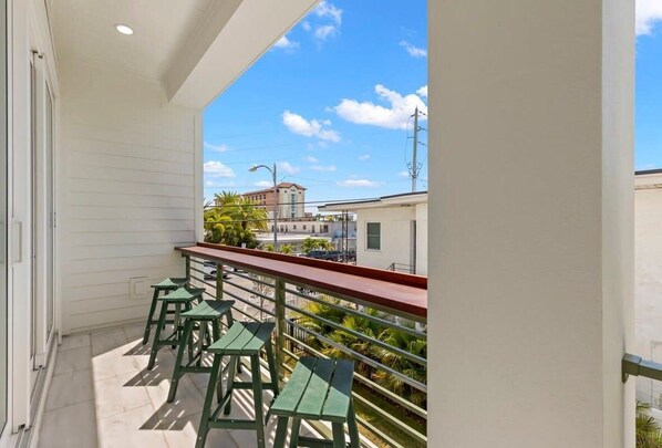 A balcony with a red railing, green chairs, and a view of buildings and palm trees.