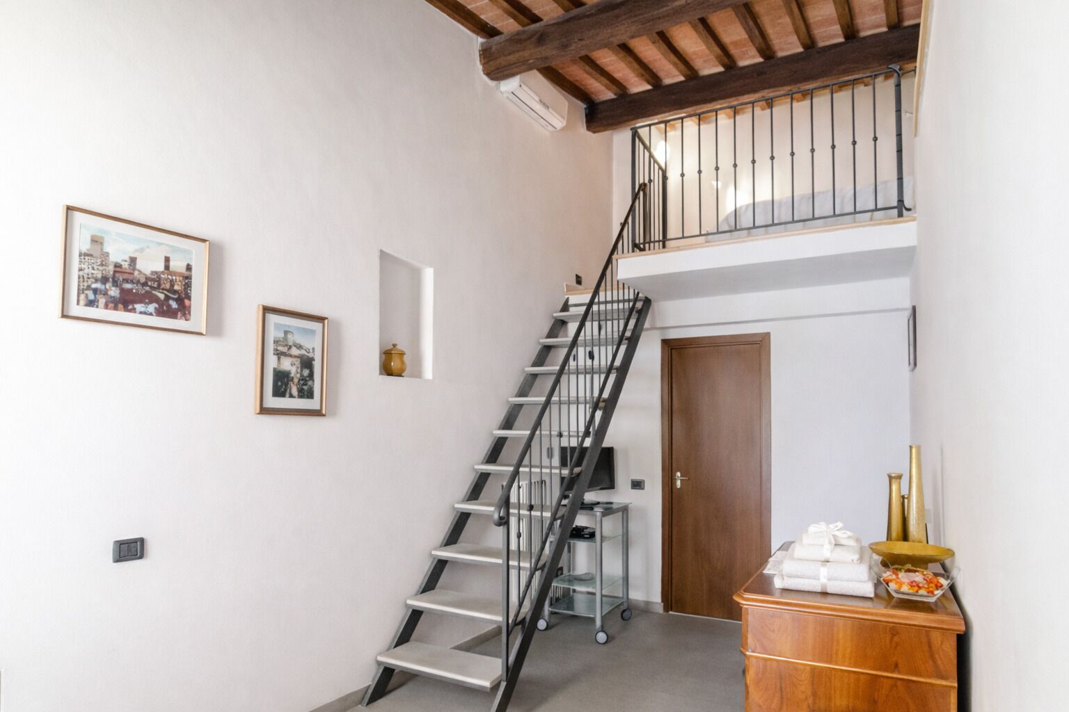 A staircase with a metal railing leading to a second floor, a wooden door, and a small table with items on it.