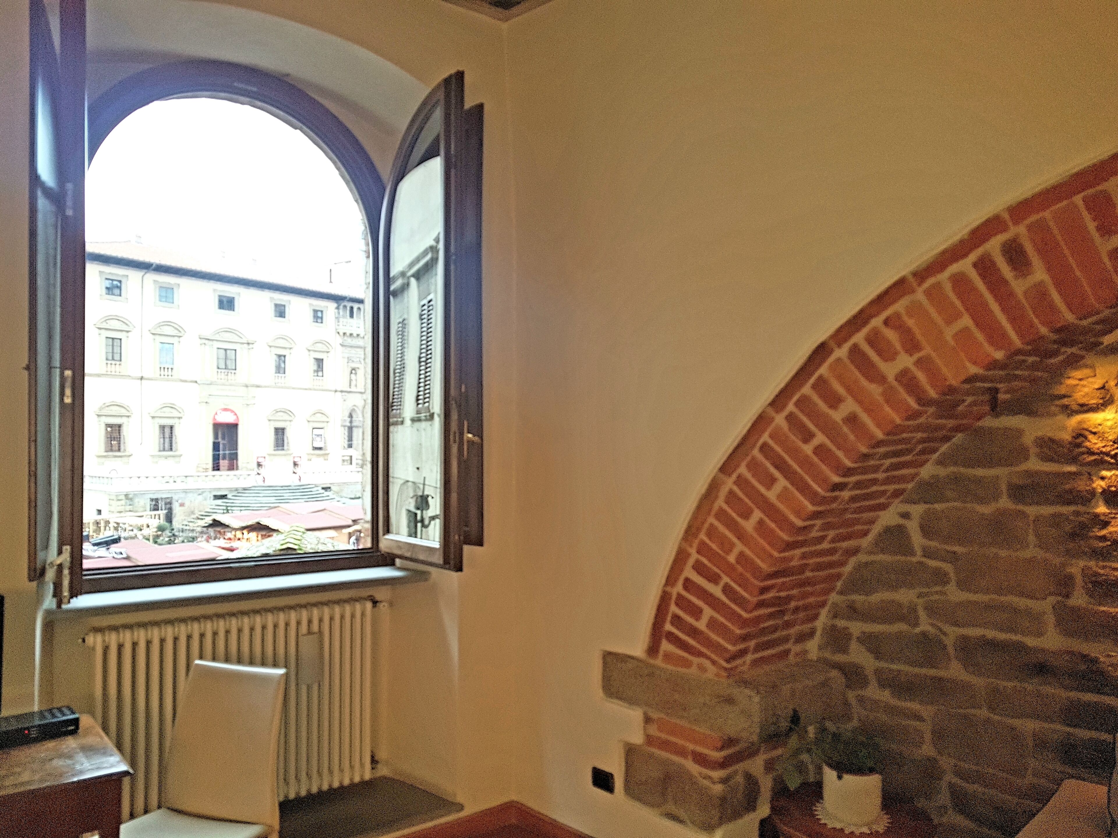A room with a large arched brick fireplace, a radiator below a window, and a view of a building outside.