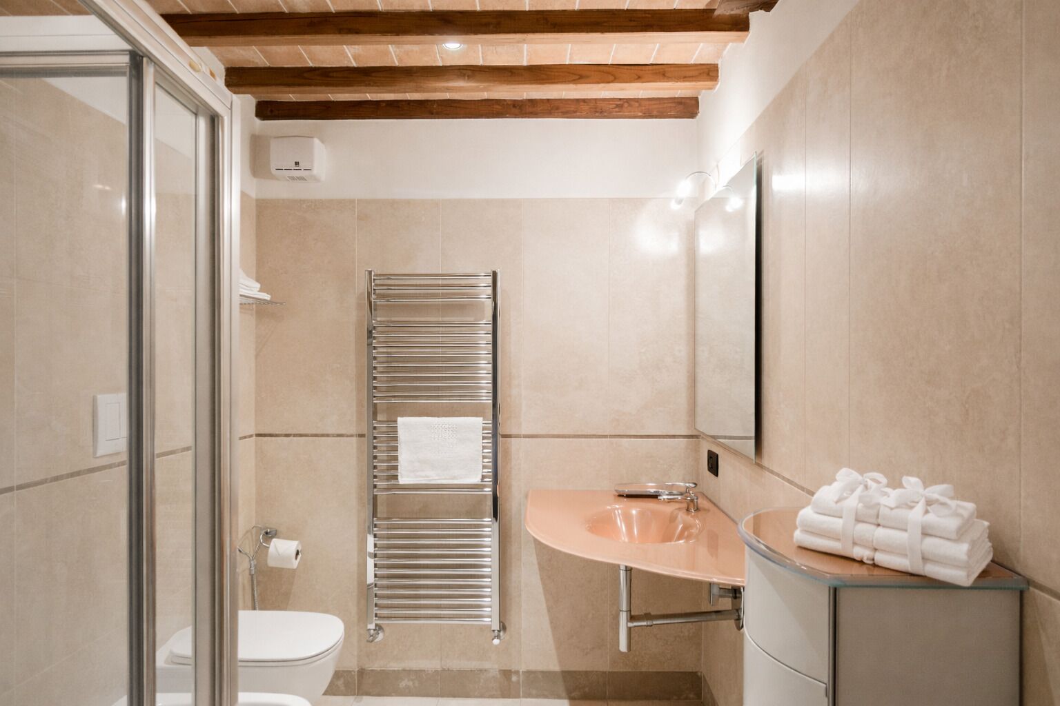 A modern bathroom with a glass shower enclosure, a built-in towel rack, a sink with a mirror, and a toilet.