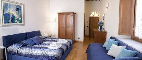 A bedroom with a bed, a sofa, a wardrobe, and a painting on the wall.
