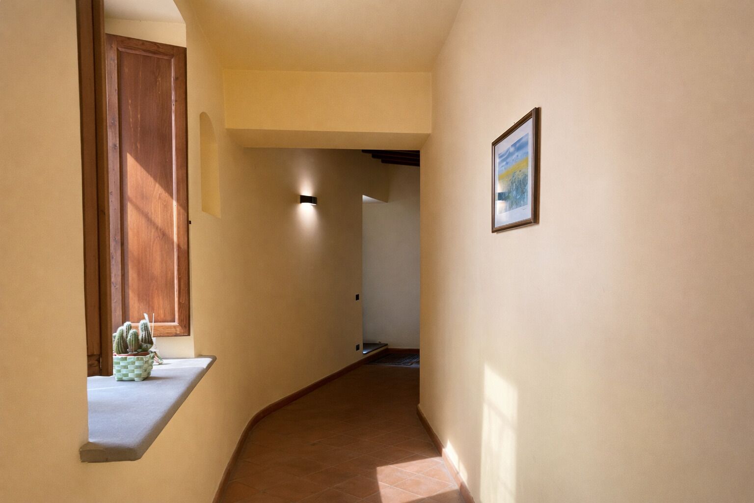 Un pasillo con una puerta de madera, una planta pequeña y un cuadro en la pared.