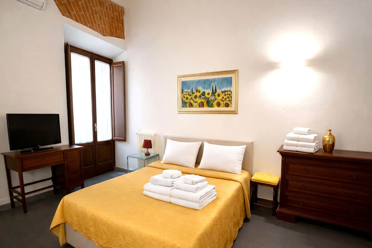 Una habitación de hotel con cama, televisión, un cuadro y cómoda con toallas.