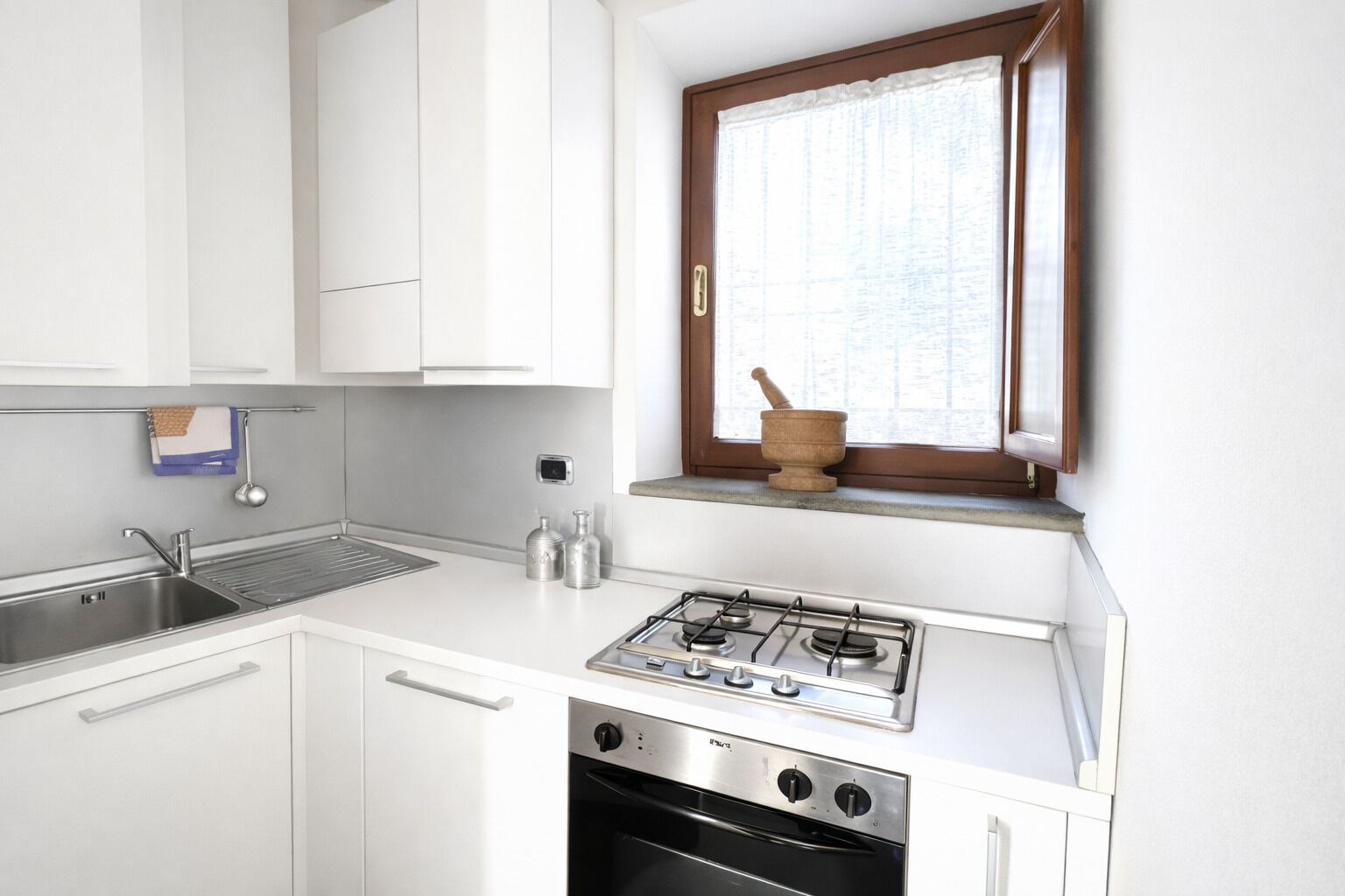 A kitchen with white cabinets, a stainless steel sink, a gas stove, and an oven.