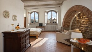 Una habitación con cama, escritorio, televisor y vistas a la ciudad a través de ventanales abovedados.