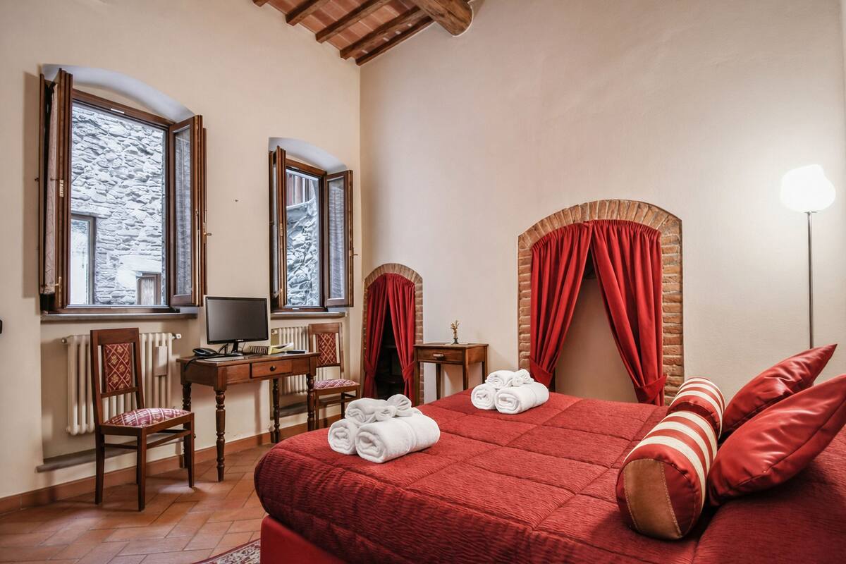 Un dormitorio con una cama grande, dos ventanas, un escritorio, una silla y un radiador.