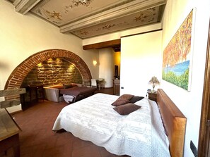 Um quarto com lareira de pedra, uma cama com colcha branca e um quadro de uma paisagem.