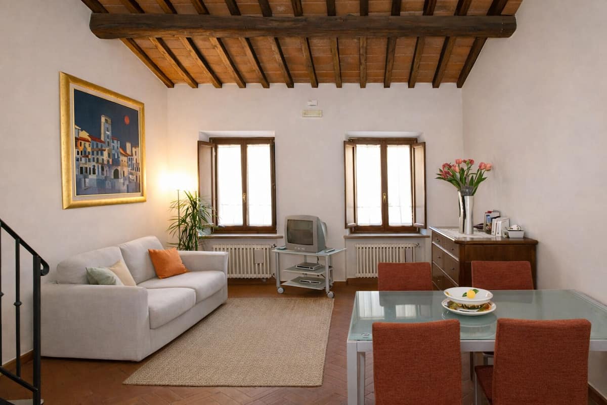 Una sala de estar con un sofá, una mesa de comedor con sillas, un televisor y un cuadro en la pared.
