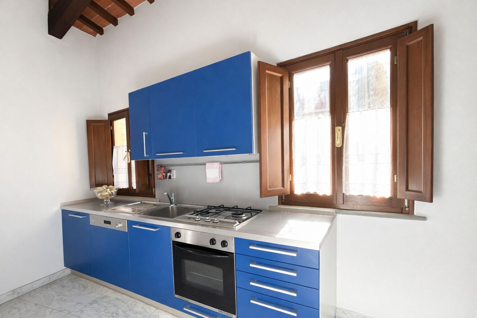 A kitchen with blue cabinets, a stainless steel stove, and a window with wooden shutters.