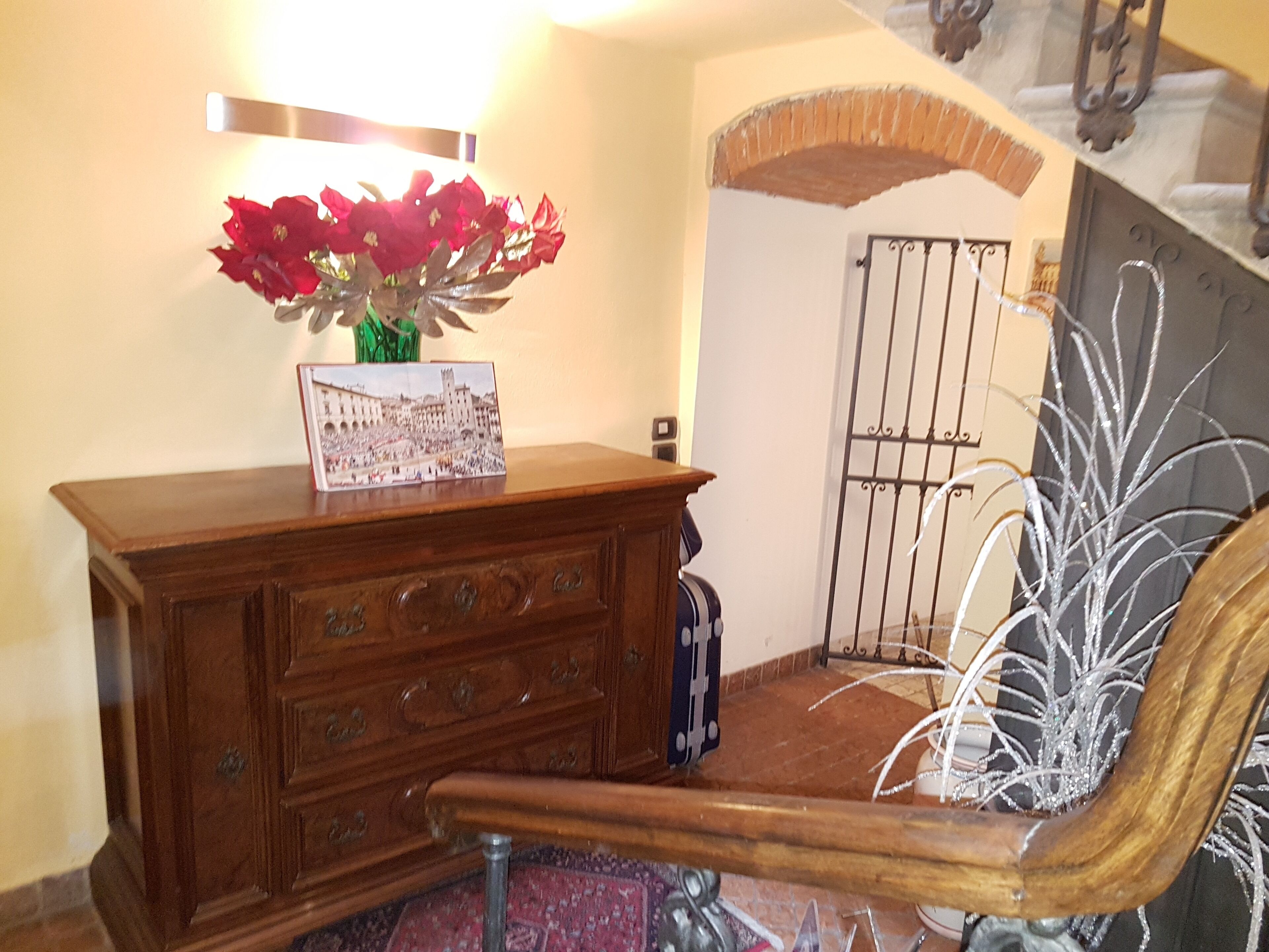 A wooden dresser with a vase of red flowers and a postcard.