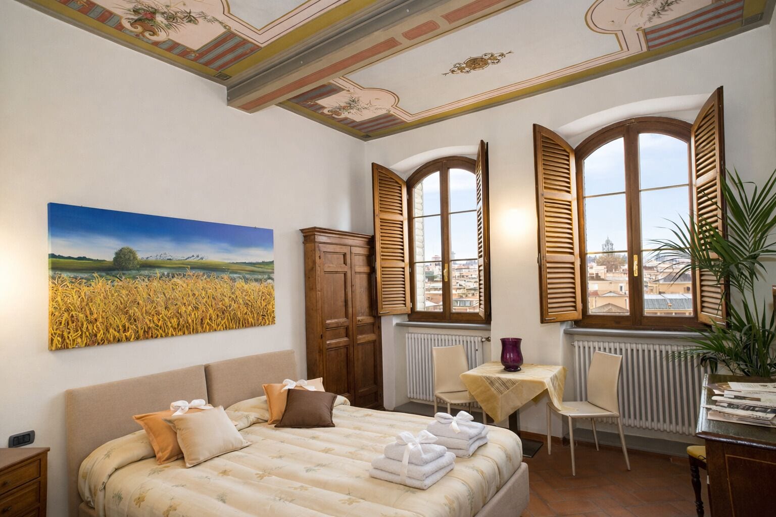 Een slaapkamer met een bed, een stoel, een tafel, een radiator en een raam met luiken.